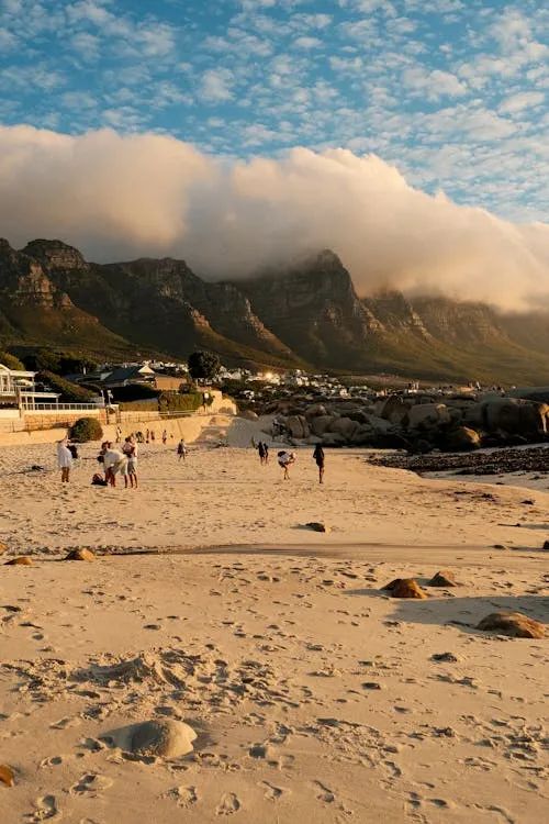 免費 人們在山巒和雲彩附近欣賞日落的海灘景色。 圖庫相片